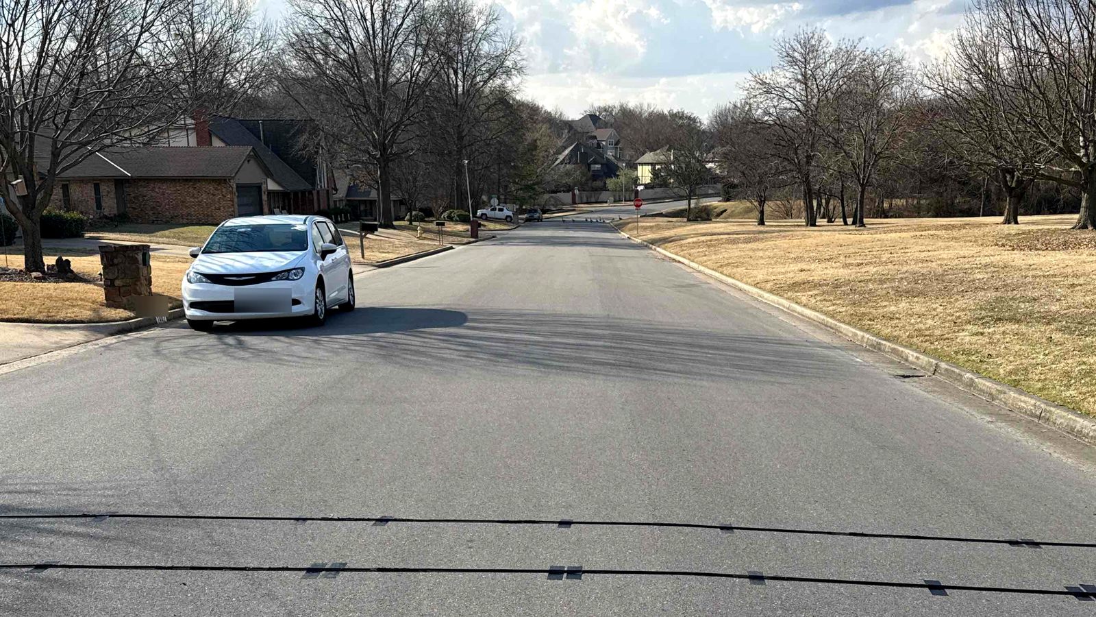 Two pneumatic road tubes fastened across a residential street in Tulsa, Oklahoma, with a parked vehicle and houses beyond